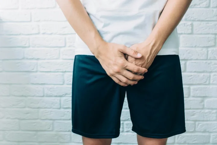 A man standing with his hands held in front of his groin.
