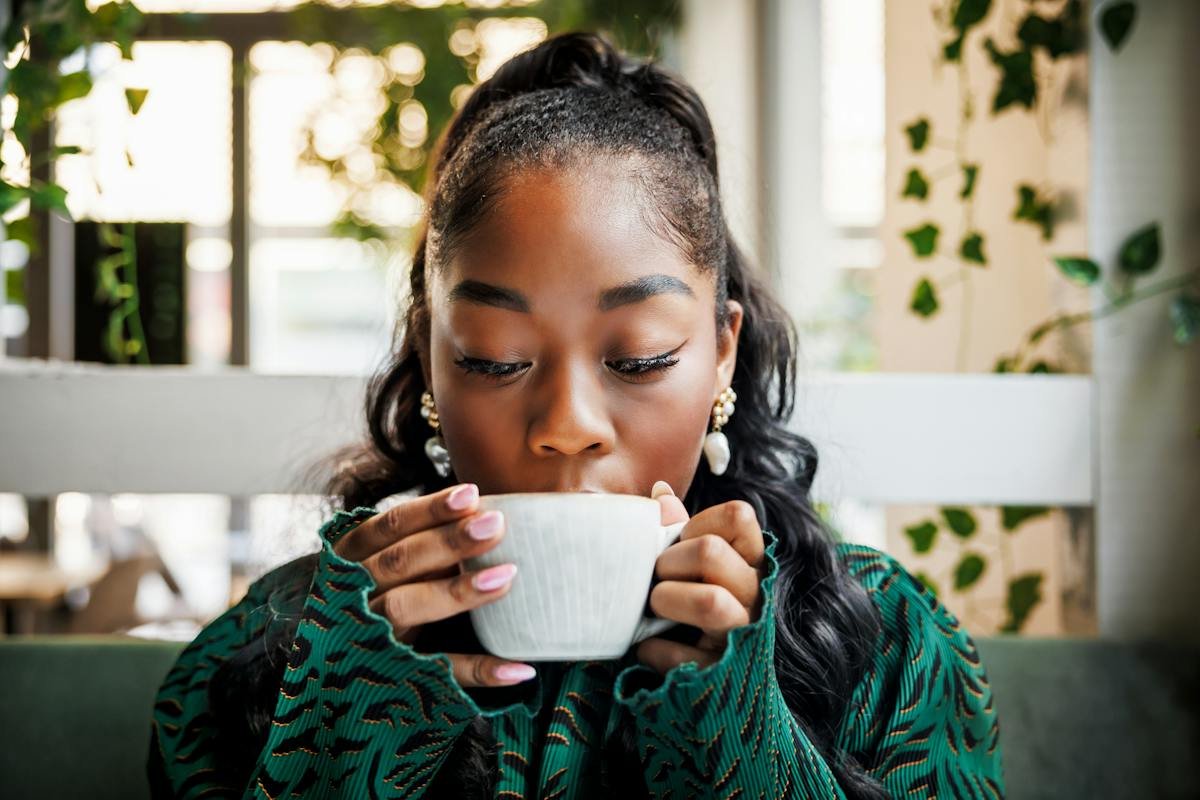 Woman drinking from a cup near a window