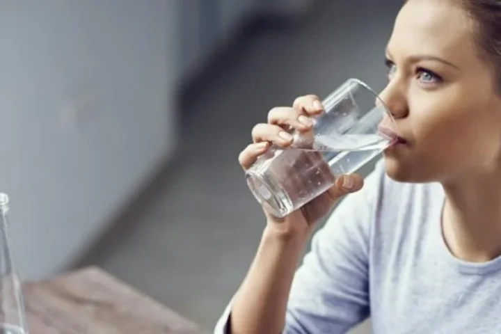 A woman drinking a glass of water while seated.