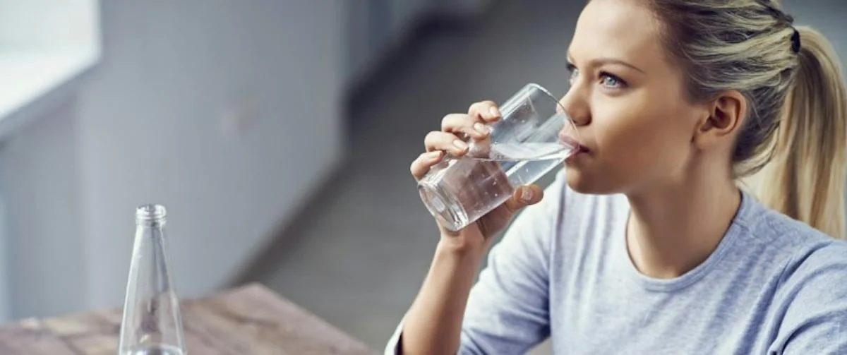 A woman drinking a glass of water while seated.