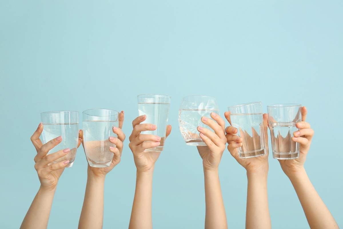 Raised hands holding glasses of water against a blue background