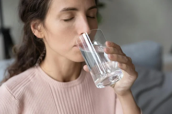 A woman drinking from a clear glass of water.
