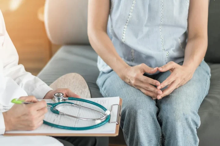 A seated patient holding her lower abdomen beside a clinician.