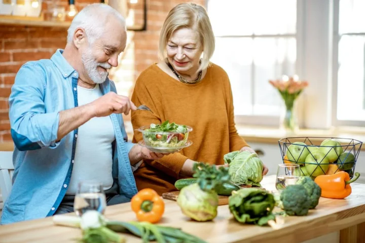An older couple preparing a salad together in a kitchen.