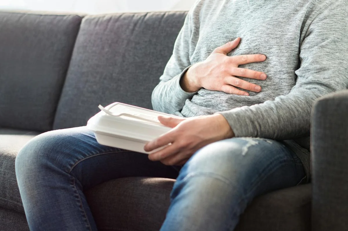 A seated person holding their upper abdomen.