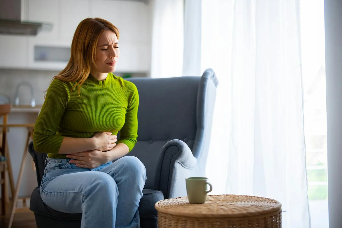 A woman seated on a sofa with her hands over her lower abdomen.