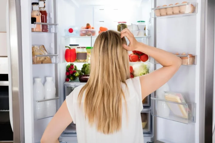 A person looking inside an open refrigerator.