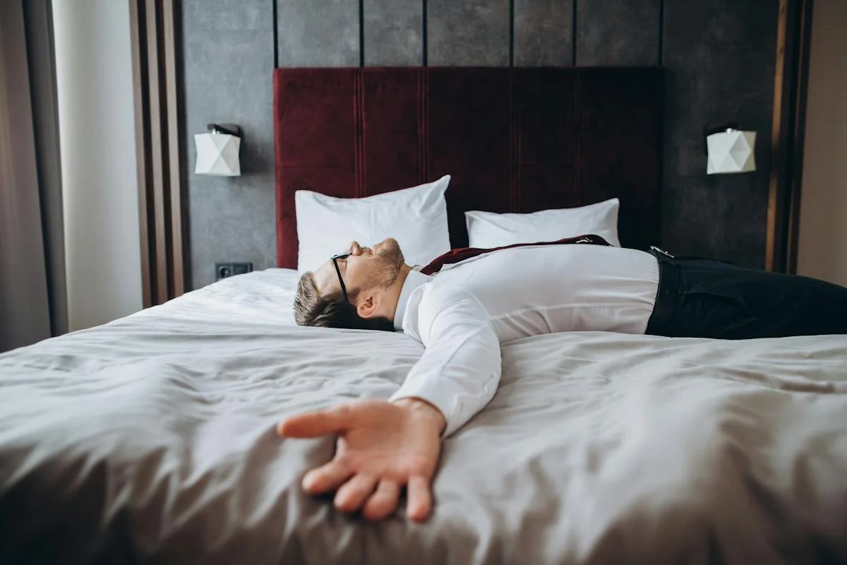 A traveler resting on a hotel bed with a suitcase nearby.