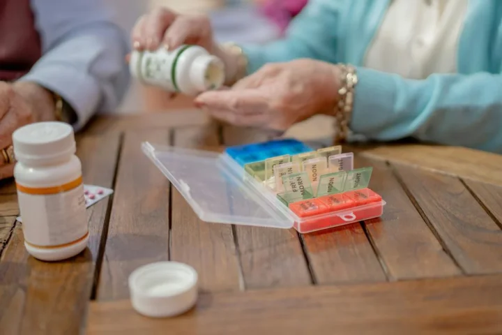 An older adult arranging medicines beside a pill organizer.