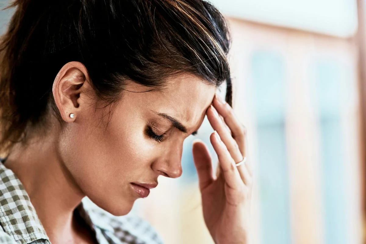 A woman holding her forehead with her eyes closed.