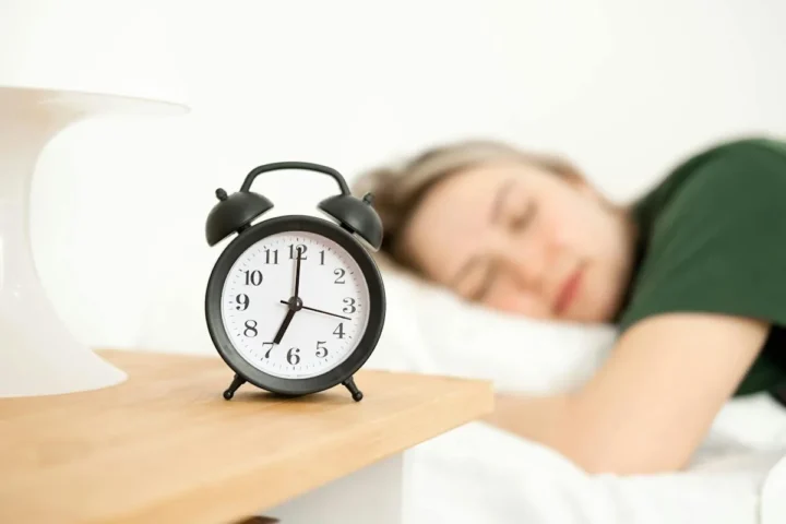 A woman resting beside an analog alarm clock.