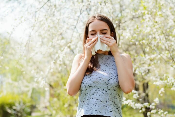 Woman holding a tissue to her nose in a flowering outdoor setting