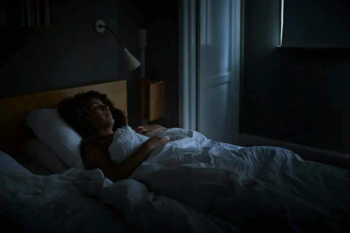 A person resting in bed in a dark bedroom.