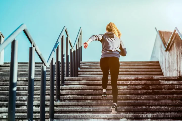 A person climbing an outdoor staircase beside a handrail.