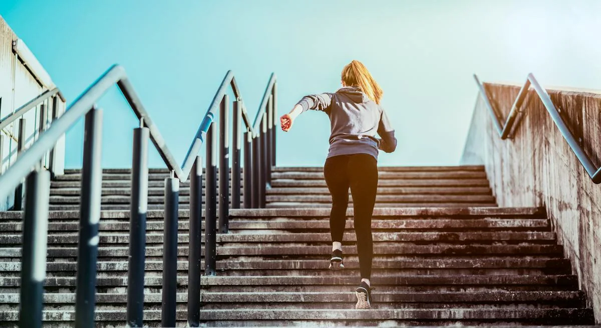 A person climbing an outdoor staircase beside a handrail.