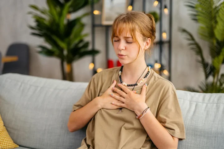 A woman sitting on a sofa with a hand on her chest.
