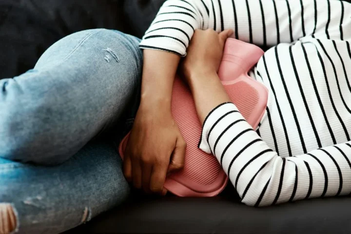 A person lying down with a hot water bottle near the abdomen.