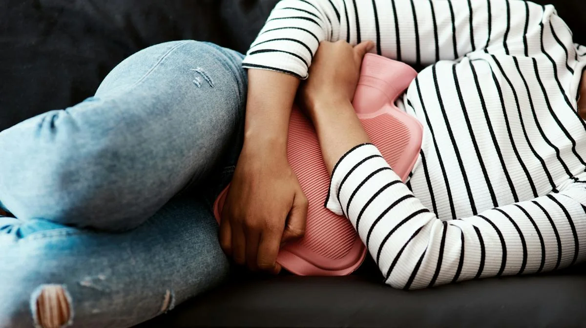 A person lying down with a hot water bottle near the abdomen.