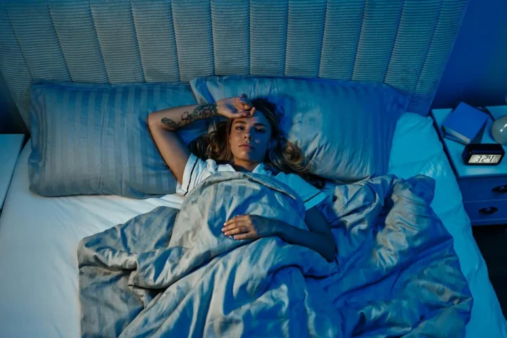 A person lying awake in a bed with rumpled bedding.
